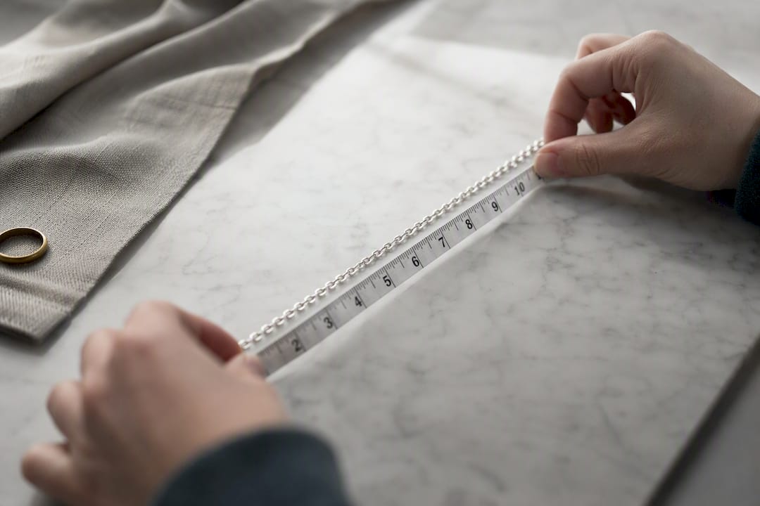 Hands measuring silver chain with tape