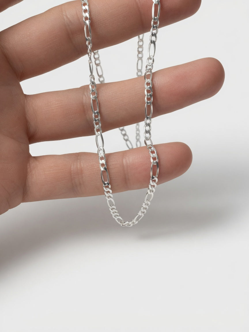 Silver figaro chain held between fingers on a white background