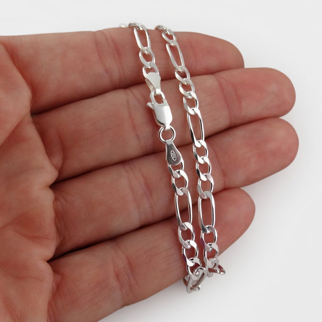 Silver figaro chain necklace held between fingers on a white background