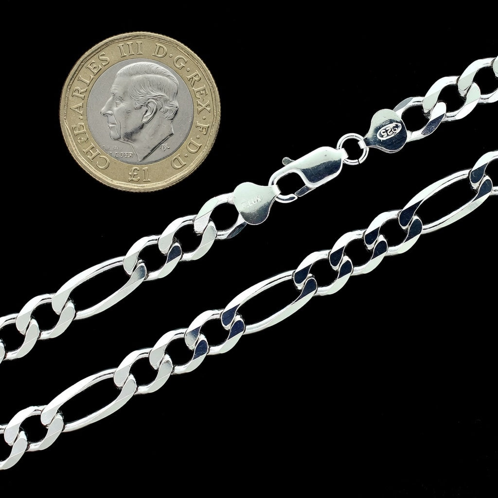 Silver figaro chain next to a British pound coin on a black background